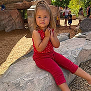 Sarah is registered to the contest to win money with this photo: blonde_hair, boulder, child, family_outing, girl, long_hair, outdoor, park, play_area, playground, portrait, red_outfit, rock, shade_sails, sitting, smiling, star_pattern, sunlight, toddler, trees