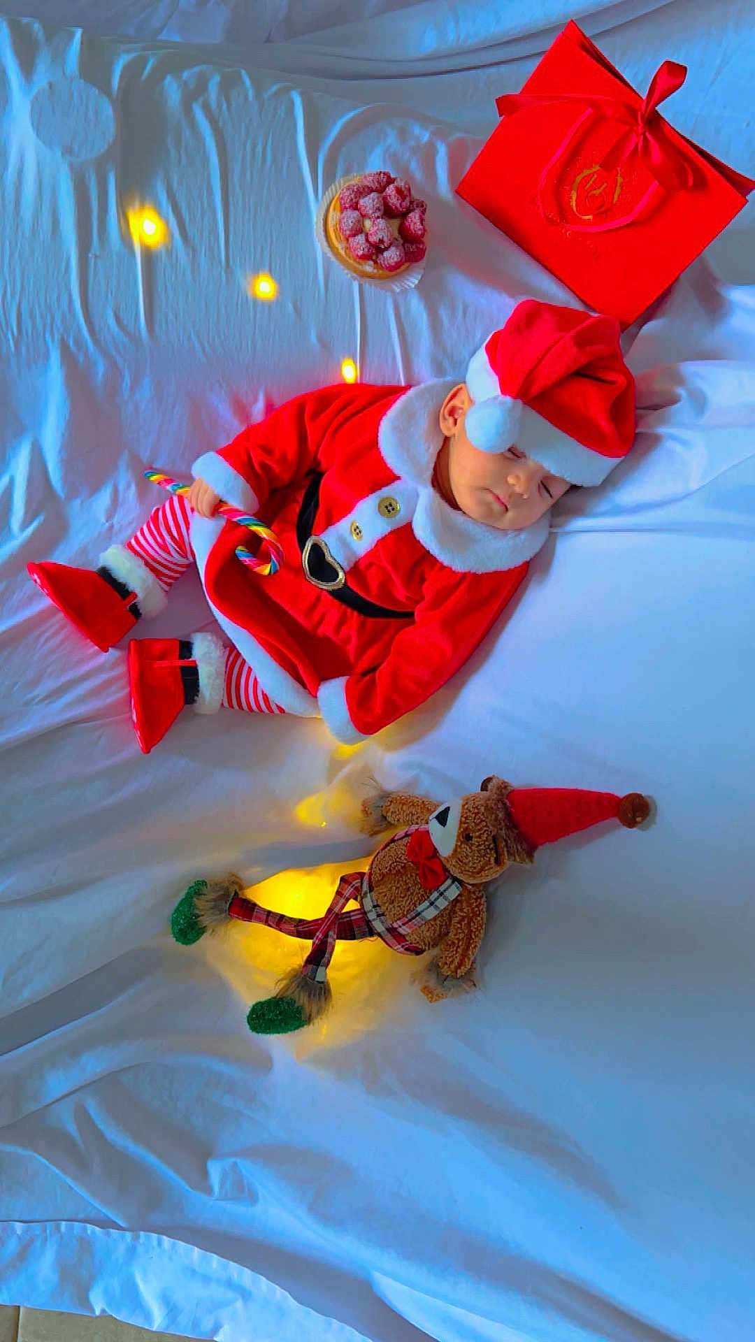 Esraa participe au concours pour gagner de l'argent avec cette photo : baby, candy_cane, child, christmas, cozy, cute, fairy_lights, festive, gift_bag, holiday, indoors, plaid_pants, red_hat, red_shoes, santa_claus_costume, sleeping, soft_lighting, teddy_bear, toy, white_bed