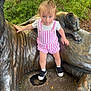 toddler, child, statue, tiger, bronze, outdoor, greenery, tree, fence, curious, clothing, pink_stripes, shoes, socks, hair, sidewalk, nature, park, person, daylight