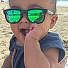 baby, child, beach, sunglasses, blue_sky, ocean, sand, outdoor, portrait, sitting, smiling, infant, fashion, reflective_lenses, sunlight, shoreline, summer, hand, clothing, family