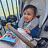 baby, child, stroller, smiling, laughing, outdoor, seaside, water, railing, fan, book, harry_potter, harness, safety_seat, infant, portrait, happy, blue_sweater, blanket, sunlight