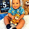 Nestor is registered to the contest to win money with this photo: baby, child, infant, smiling, happy, portrait, sitting, tiger_plushie, teddy_bear, stuffed_animal, chalkboard, five_months, curly_hair, blue_outfit, patterned_clothing, sneakers, indoor, blanket, nursery, celebration