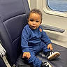 baby, child, toddler, train, train_interior, seated, blue_outfit, knitwear, sneakers, seatbelt, window, passenger, portrait, curly_hair, looking_at_camera, indoors, travel, transportation, leather_seat, safe_travel