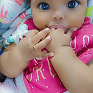 Laylani joined the competition — help win amazing prizes! baby, child, infant, face, hand, bib, clothing, cute, close_up, indoors, patterned_clothes, colorful, skin, person, chewing, sitting, soft_background, floral_pattern, portrait, young