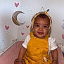 baby, child, smiling, yellow_overall, headband, pink_socks, bracelets, indoor, wall_decor, hearts, stars, moon, cloud, cute, portrait, sitting, infant, happy, face, clothing