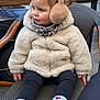 toddler, child, earmuffs, winter_jacket, scarf, white_sneakers, heart_socks, outdoor, chair, woven_chair, street, curious, cute, fashion, warm_clothing, daylight, casual, sitting, young_child, portrait
