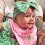 adult, baby, blue_eyes, bow, closeup, clothing, cute, face, headband, holding, ice_cream_cone, indoor, infant, person, pink_bib, portrait, skin, smile, tattoo, tshirt