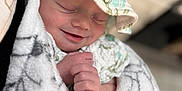 Mclane is registered to the contest to win money with this photo: baby, newborn, smiling, sleeping, blanket, hat, closeup, infant, soft_texture, wrapped, cute, peaceful, hand, cozy, portrait, indoors, child, face, resting, comfort