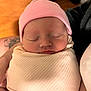 Mclane is registered to the contest to win money with this photo: newborn, baby, sleeping, pink_hat, blanket, swaddled, infant, face, closed_eyes, soft, cute, person, hand, skin, cozy, indoor, warm_colors, wood_floor, tattoo, resting
