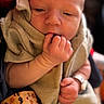baby, newborn, infant, child, portrait, face, hands, finger, sucking_finger, blanket, wrapped, cozy, seated, close_up, indoor, soft_lighting, warm_tones, photography, baby_clothing, peaceful