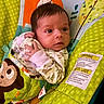 baby, infant, blanket, monkey, pattern, green, cushion, warning_label, clothing, hand, face, eyes, curious, alert, indoors, colorful, fabric, soft_toys, child, portrait
