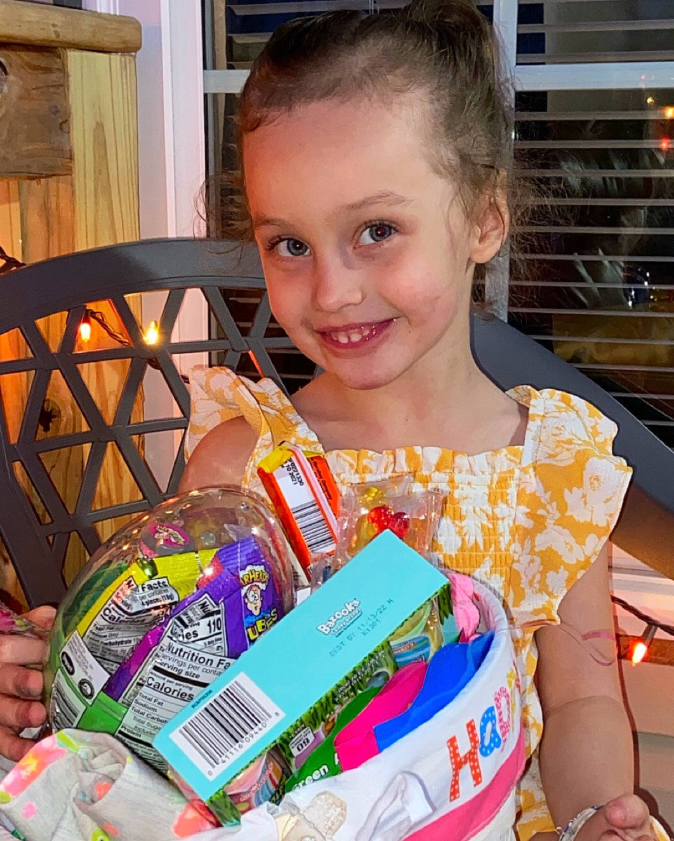 Elizabeth joined the competition — help win amazing prizes! basket, box, child, convenience_food, event, facial_expression, fun, happy, holiday, joy, packaging_and_labeling, packing_materials, pattern, person, plastic, present, service, sitting, smile, sweetness