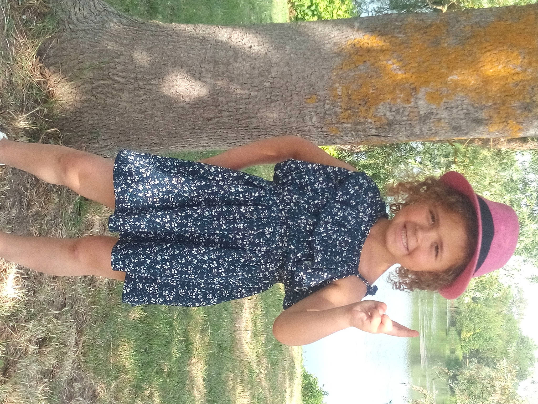 Liliana participe au concours pour gagner de l'argent avec cette photo : barefoot, child, cool, face, fun, grass, happy, hat, headwear, human_leg, joy, leisure, pattern, people_in_nature, person, smile, t_shirt, thigh, tree, trunk
