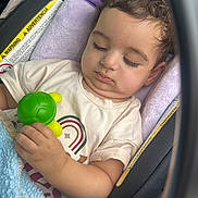Wadie is registered to the contest to win money with this photo: baby, sleeping, car_seat, infant, toy, turtle_toy, blanket, blue_blanket, vehicle, portrait, child, peaceful, cozy, seated, curly_hair, closed_eyes, casual_clothing, indoors,  안전, photograph