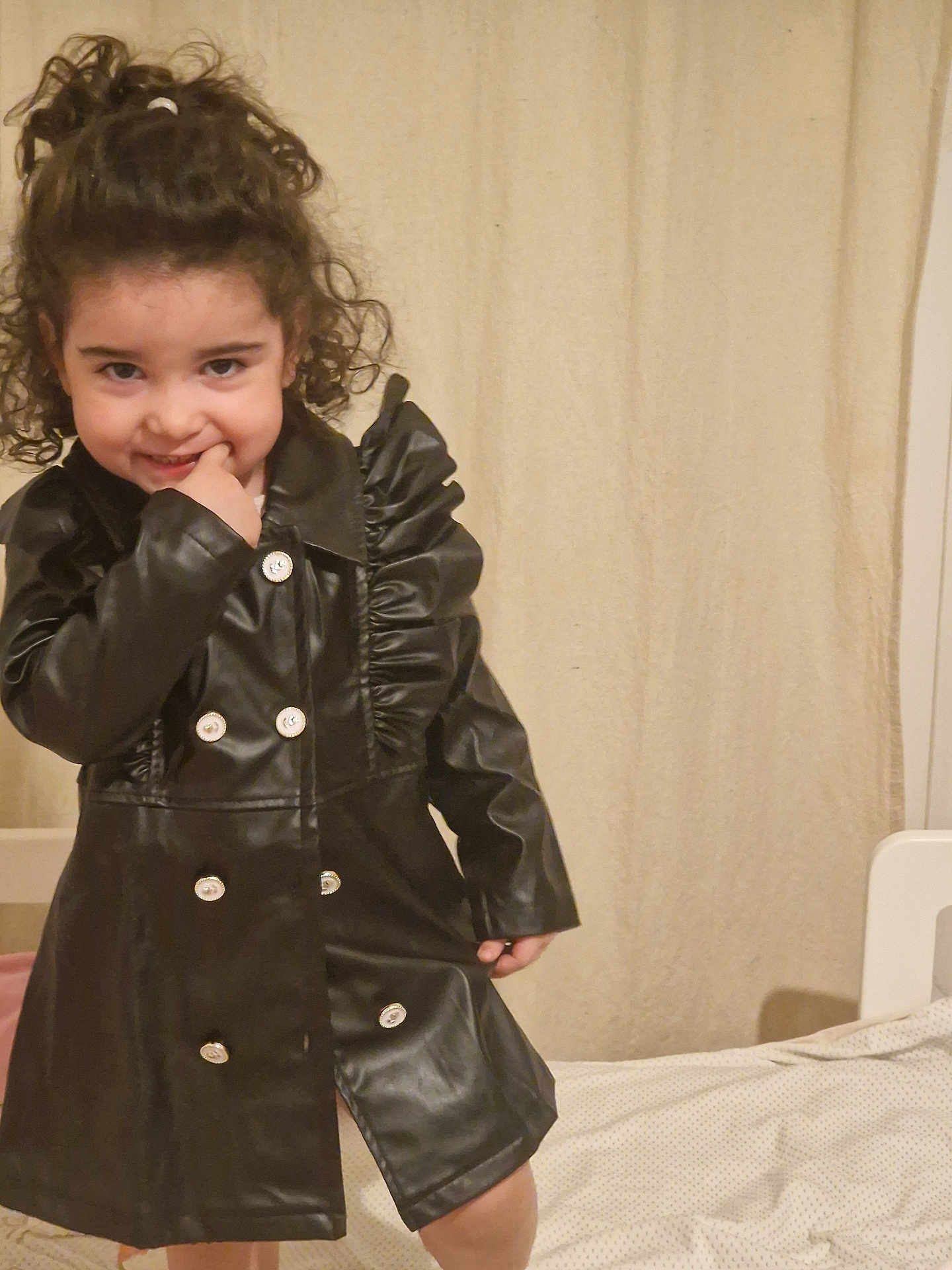 Gioia Maria participe au concours pour gagner de l'argent avec cette photo : child, curly_hair, black_coat, indoor, bed, smiling, playful, person, curtain, buttoned_coat, fashion, cute, portrait, young, happy, standing, fingertip, light_skin, casual, room