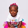 accessory, birthday, braided_hair, bright_colors, celebration, chair, child, colorful_tutu, cute, fashion, gold_bracelet, happy, pink_bow, portrait, posing, smiling, studio_photo, toddler, white_background, white_shirt