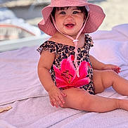 Amaia joined the competition — help win amazing prizes! baby, child, smile, pink_hat, swimsuit, flower_print, leopard_print, towel, outdoor, beach, sunhat, happy, sitting, cute, portrait, young_child, summer, sunny, playful, person