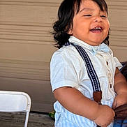 Caleb Paz is registered to the contest to win money with this photo: toddler, child, smiling, happy, white_shirt, suspenders, short_sleeves, dark_hair, indoor, person, cute, young_child, portrait, baby, chubby_cheeks, standing, casual_clothing, background, chair, laughing
