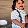 toddler, child, smiling, happy, white_shirt, suspenders, short_sleeves, dark_hair, indoor, person, cute, young_child, portrait, baby, chubby_cheeks, standing, casual_clothing, background, chair, laughing