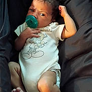 Osiris is registered to the contest to win money with this photo: baby, infant, child, portrait, pacifier, blanket, bed, lying_down, sitting, white_onesie, clothing, dark_background, face, eyes, hair, arm, legs, feet, indoor, relaxed