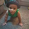 arm, baby, carpet, child, crawling, curious, face, floor, furniture, green_shirt, hat, headwear, home, indoor, person, play, smile, toddler, toy, young_child