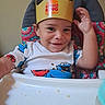 baby, burger_king_crown, child, clothing, colorful, cute, face, food_crumbs, hand, happy, high_chair, indoor, messy, person, portrait, seat, smiling, toddler, tray, young_child