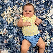 Rane joined the competition — help win amazing prizes! baby, smile, yellow_top, blue_shorts, rug, patterned_rug, child, infant, happy, lying_down, cute, cheerful, skin, legs, hands, indoors, floor, portrait, casual_clothing, young_child