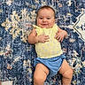 baby, smile, yellow_top, blue_shorts, rug, patterned_rug, child, infant, happy, lying_down, cute, cheerful, skin, legs, hands, indoors, floor, portrait, casual_clothing, young_child