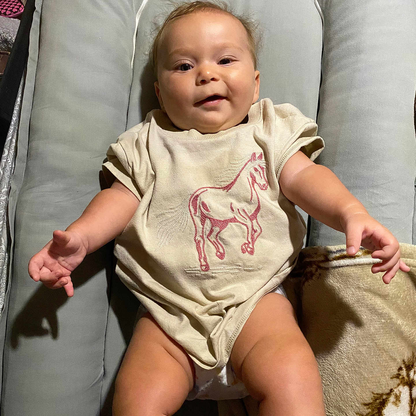 Rane joined the competition — help win amazing prizes! baby, infant, child, smiling, cute, sitting, clothing, shirt, horse_design, blanket, cushion, indoor, furniture, person, face, head, legs, arms, happy, skin