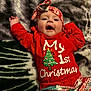 Maria is registered to the contest to win money with this photo: baby, child, infant, red_clothing, headband, christmas, holiday, smiling, lying_down, blanket, patterned_pants, happy, cute, festive, celebration, indoors, portrait, face, person, cozy