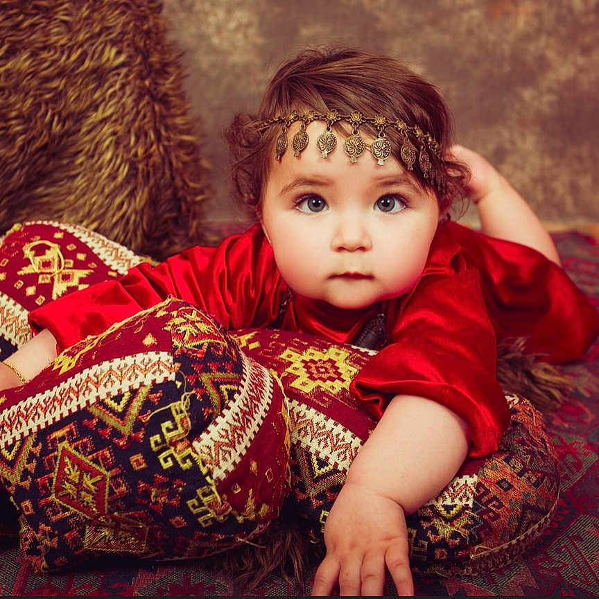 Milena participe au concours pour gagner de l'argent avec cette photo : baby, carpet, child, cozy, cushions, decorative, expression, face, furniture, hand, headpiece, indoors, ornamental, patterned_fabric, portrait, red_clothing, soft_lighting, texture, traditional, young_child
