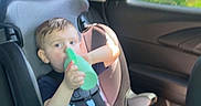 Levi is registered to the contest to win money with this photo: child, car_seat, sippy_cup, car_interior, seatbelt, window, green, shorts, tshirt, shoes, sunlight, trees, road_trip, young_child, sitting, vehicle, safety, casual, daytime, cute