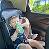child, car_seat, sippy_cup, car_interior, seatbelt, window, green, shorts, tshirt, shoes, sunlight, trees, road_trip, young_child, sitting, vehicle, safety, casual, daytime, cute