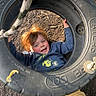 child, tire_swing, playground, smiling, red_hair, rope, outdoor, wood_chips, blue_sweater, yellow_pants, happy, play, fun, person, recreation, childhood, leisure, casual_clothing, daylight, ground