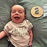 baby, infant, smiling, happy, clothing, shirt, text, wooden_sign, months, blanket, fabric, texture, person, portrait, cute, child, lying_down, indoors, young, face