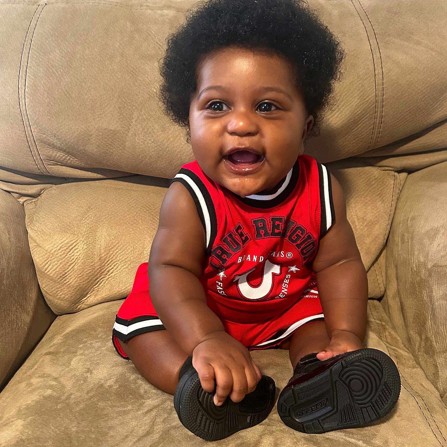 Tripp joined the competition — help win amazing prizes! baby, child, smiling, curly_hair, red_outfit, sitting, couch, indoor, cute, happy, black_shoes, portrait, infant, plush, furniture, person, young_child, head, face, apparel