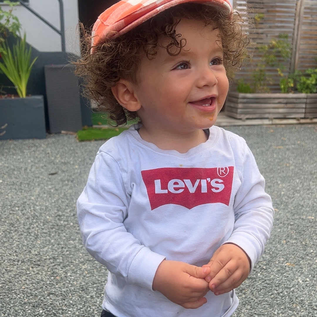Eymen a rejoint le concours — aidez-le/la à gagner de superbes lots ! building, cap, casual_clothing, child, curly_hair, curly_hair_kid, daylight, fence, gravel, happy, levis, orange_cap, outdoor, plants, portrait, smile, standing, toddler, white_shirt, young_child