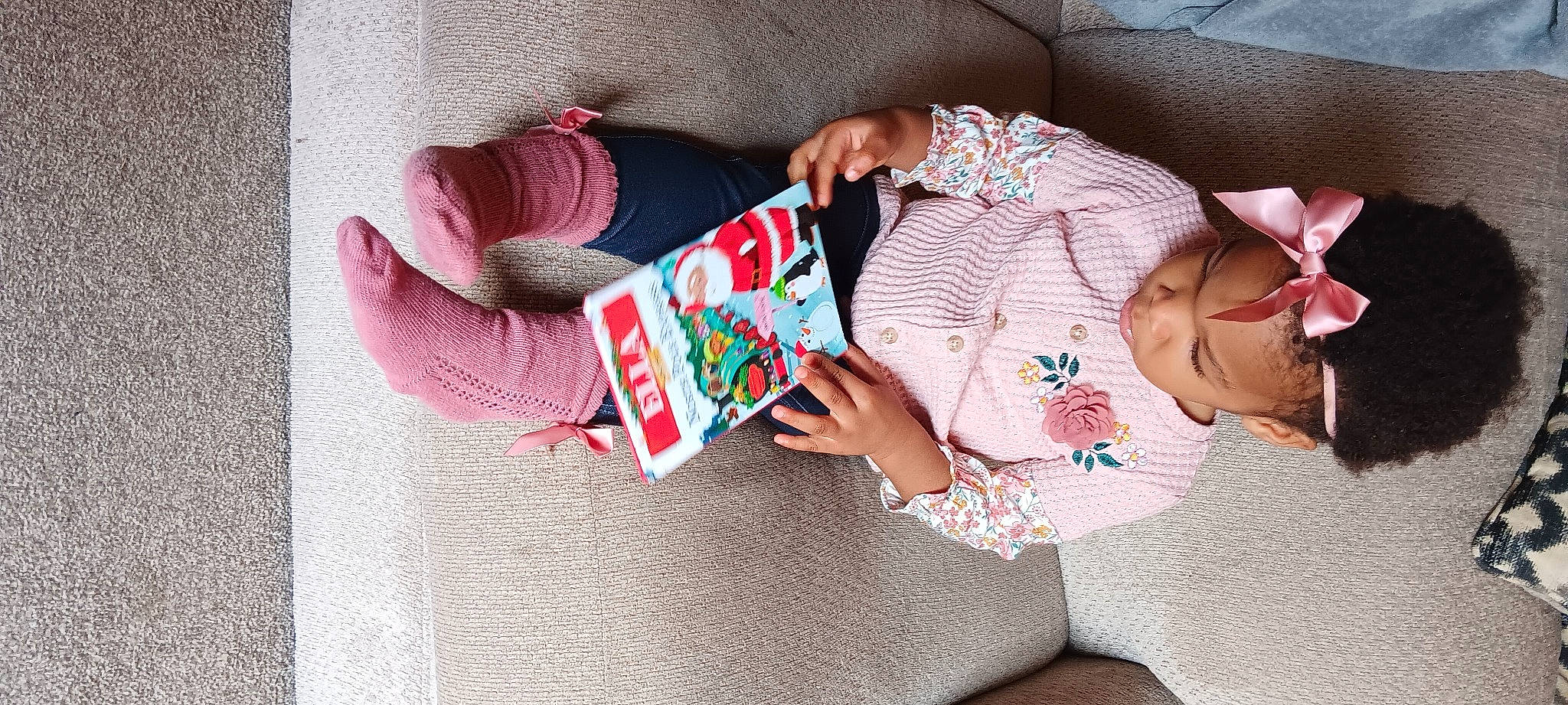 Ella is registered to the contest to win money with this photo: arm, art, baby_toddler_clothing, book, child, comfort, finger, hand, human_body, leg, linens, nail, pattern, person, pink, publication, sitting, sleeve, textile, toddler