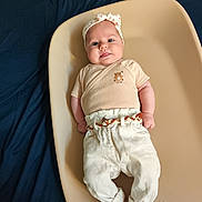 Mia a rejoint le concours — aidez-le/la à gagner de superbes lots ! baby, infant, headband, clothing, pants, belt, changing_pad, blue_background, person, face, tongue, cute, chubby_cheeks, sitting, laying_down, fabric, soft_lighting, portrait, newborn, child