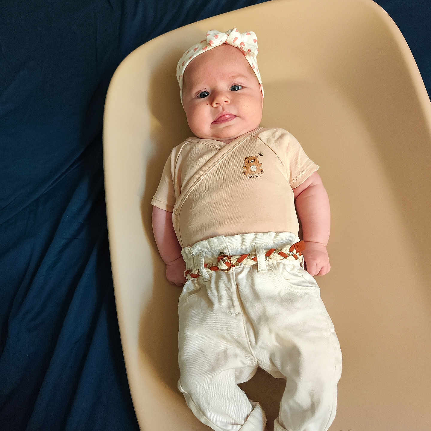Mia a rejoint le concours — aidez-le/la à gagner de superbes lots ! baby, infant, headband, clothing, pants, belt, changing_pad, blue_background, person, face, tongue, cute, chubby_cheeks, sitting, laying_down, fabric, soft_lighting, portrait, newborn, child