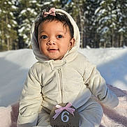 Caleigh is registered to the contest to win money with this photo: baby, blanket, blue_sky, child, cold, cute, face, forest, hood, infant, onesie, outdoor, pink_bow, portrait, sign, sitting, smiling, snow, trees, winter