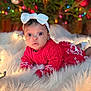 baby, infant, red_sweater, white_bow, christmas_tree, ornaments, holiday_lights, fluffy_rug, cute, curious, indoors, festive, decorations, child, christmas, winter_clothing, portrait, holiday_season, smiling, seasonal