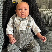 Reuben joined the competition — help win amazing prizes! baby, infant, child, boy, clothing, bow_tie, suspenders, shirt, pants, socks, couch, pillow, indoor, portrait, sitting, cute, face, expression, home, furniture