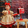 toddler, child, dress, red_bow, headband, mailbox, christmas, holiday, decor, red_shoes, wooden_floor, wooden_table, brick_wall, window, curious, indoor, portrait, festive, cute, person