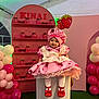toddler, child, pink_dress, strawberry_theme, hat, red_shoes, balloons, pedestal, smiling, party, decoration, festive, indoor, celebration, girl, costume, cute, face, portrait, colorful
