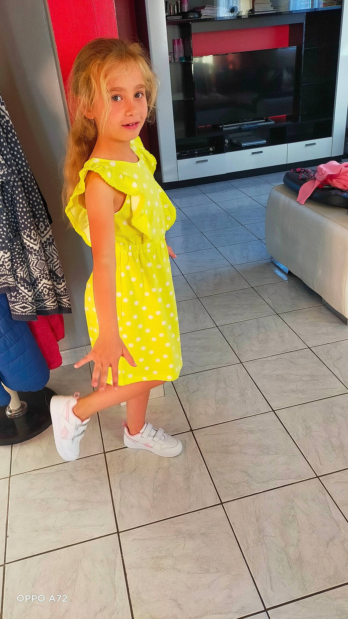 Victoria participe au concours pour gagner de l'argent avec cette photo : dress, entertainment_center, eye, floor, flooring, fun, hairstyle, joint, leg, one_piece_garment, person, sandal, shoe, skin, sneakers, standing, television, thigh, toddler, waist