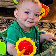 Soran is registered to the contest to win money with this photo: baby, child, toddler, smiling, portrait, face, green_shirt, activity_center, toy, colorful, lion_toy, flower_toy, indoor, seated, playtime, carpet, furniture, happy, closeup, photography
