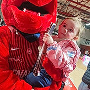 Eliana a rejoint le concours — aidez-le/la à gagner de superbes lots ! child, mascot, red_costume, sports_arena, basketball_court, person, holding, paper, curious, costume, indoor, event, people, clothing, blue_leggings, pink_jacket, fun, entertainment, fan, mascot_character
