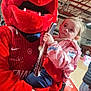 child, mascot, red_costume, sports_arena, basketball_court, person, holding, paper, curious, costume, indoor, event, people, clothing, blue_leggings, pink_jacket, fun, entertainment, fan, mascot_character