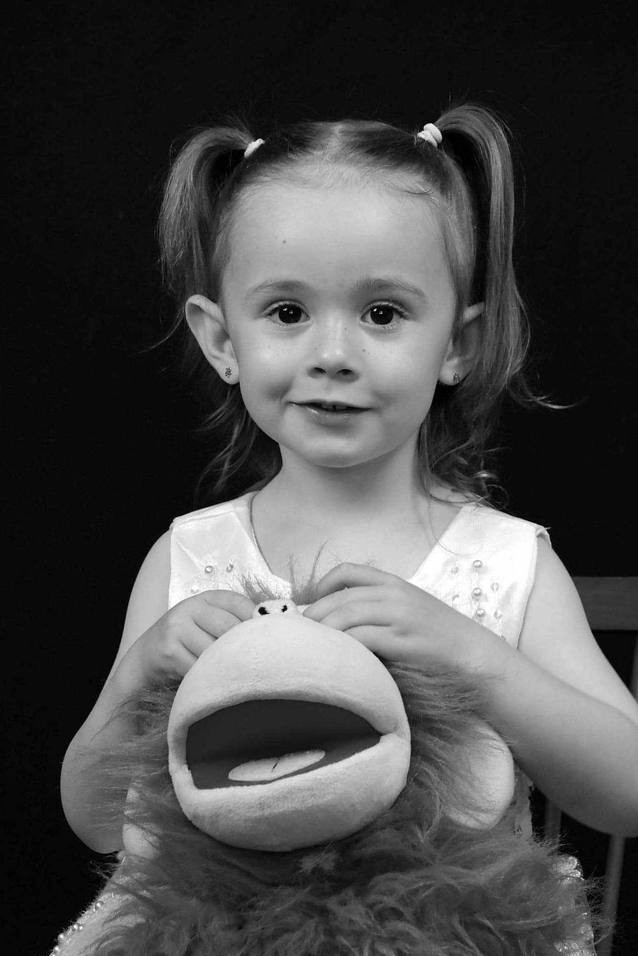 Eliana participe au concours pour gagner de l'argent avec cette photo : child, girl, pigtails, smile, puppet, stuffed_toy, portrait, black_background, cute, young, happy, holding, doll, face, eyes, hair, clothing, person, studio, expression